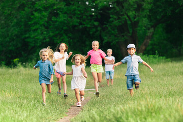 Obraz premium Kids, children running on meadow in summer's sunlight. Look happy, cheerful with sincere bright emotions. Cute caucasian boys and girls. Concept of childhood, happiness, movement, family and summer.