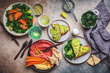 Vegan lunch table, top view. Flat-lay of baked sweet potato salad, avocado toasts and hummus on dark background. Plant based food concept.