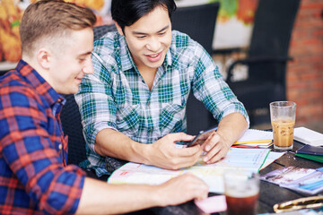 Multi-ethnic young people having coffee in coffeeshop and discussing photos from summer vacation on smartphone