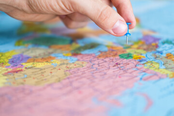 Man pins a new destination on a world map, for his next trip. Travel destination, pin on the map. Very selective focus, blur on all edges and special lightening. Hand making pin mark.