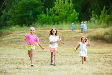 Kids, children running on meadow in summer's sunlight. Look happy, cheerful with sincere bright emotions. Cute caucasian boys and girls. Concept of childhood, happiness, movement, family and summer.