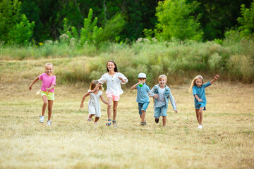 Kids, children running on meadow in summer's sunlight. Look happy, cheerful with sincere bright emotions. Cute caucasian boys and girls. Concept of childhood, happiness, movement, family and summer.