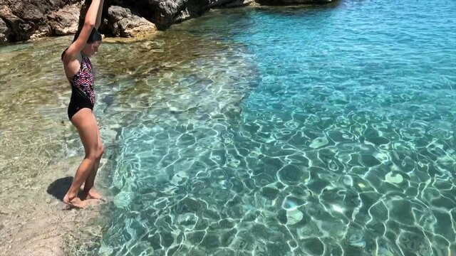 Brave young woman jumping off a cliff into the clear sea bay close-up in slow motion
