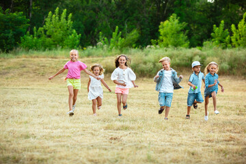 Obraz premium Kids, children running on meadow in summer's sunlight. Look happy, cheerful with sincere bright emotions. Cute caucasian boys and girls. Concept of childhood, happiness, movement, family and summer.