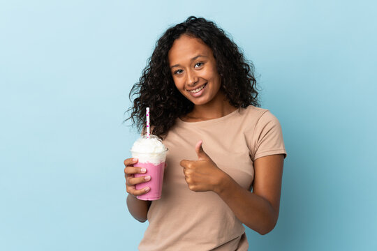 Teenager girl  with strawberry milkshake isolated on blue background giving a thumbs up gesture