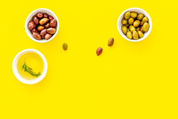 Olive oil in bowl near oilves on yellow desk from above copy space