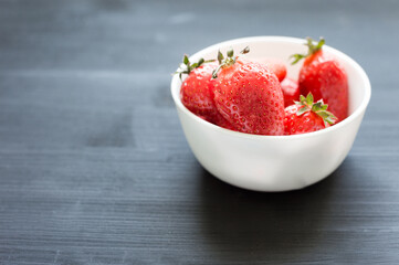 Fresh summer strawberry in the small white bowl on the black wooden backround