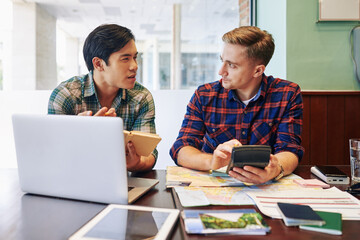 Obraz premium Multi-ethnic friends sitting at table, planning trip and calculating expences