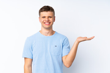Young handsome man over isolated white background holding copyspace imaginary on the palm to insert...