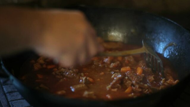 The cook prepares bograch soup in a cauldron in nature. A male hand stirs a dish in a cauldron.