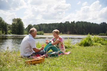  lovely senior couple  having a picnic, drink rose wine on the shore of the lake on a summer day....