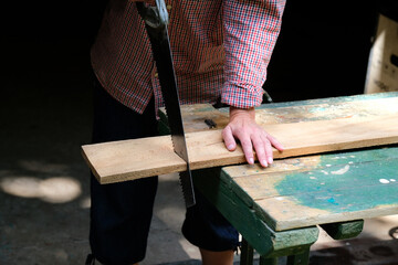 Female carpenter cutting plank using hand saw. DIY, woodwork concept.