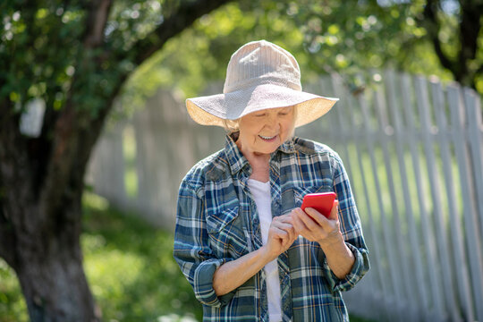 Elderly woman using a smartphone in the garden - Powered by Adobe