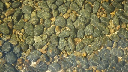 Clean round stones clearly visible in crystal water. From above clean crystal water and round grey yellow pebbles on seaside bottom or mountain river in Thailand. Natural background