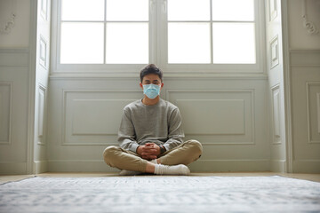 young asian man in isolation sitting on floor wearing mask