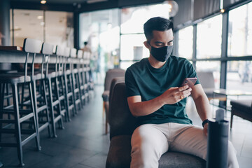 Attractive asian businessman with mask using smartphone at cafe. Drinking coffee and surfing the internet and read news. social distancing concept.