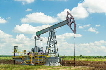 Oil pump in the field, beautiful blue sky with clouds. Russian oil production