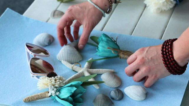 Close up hands of the wedding decorator collect a composition of sea shells and turquoise flowers. A beautiful place for wedding rings. Creative work for photography. Perfect background for rings 4k