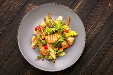 Seafood salad with grilled squid, corn, carrots, tomatoes and lettuce, on a gray plate, on a wooden background © pobaralia