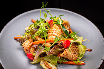 Seafood salad with grilled squid, corn, carrots, tomatoes and lettuce, on a gray plate, on a black background © pobaralia