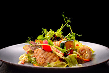 Seafood salad with grilled squid, corn, carrots, tomatoes and lettuce, on a gray plate, on a black background © pobaralia