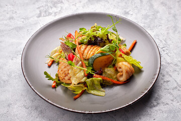 Seafood salad with grilled squid, corn, carrots, tomatoes and lettuce, on a gray plate, on a light background © pobaralia