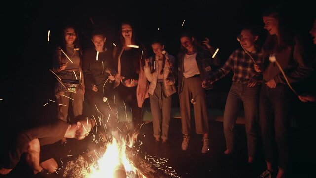 Teens roasting marshmallows on campfire.