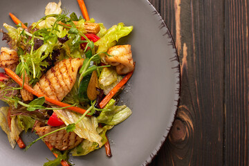 Seafood salad with grilled squid, corn, carrots, tomatoes and lettuce, on a gray plate, on a wooden background © pobaralia
