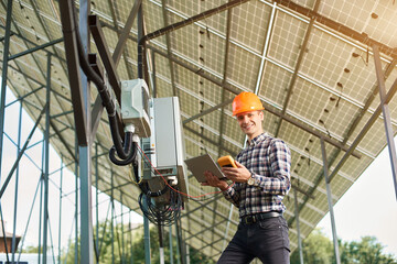 Happy man checking the operation with laptop and sensor, on the background of the solar power station. Solar panels, sunny power electricity. Innovation future. Modern technology.