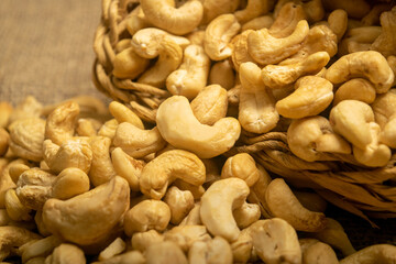 Cashew nuts in a wicker basket and cashew nuts scattered on burlap with a rough texture surface texture. Close up.
