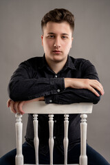 Close-up portrait of serious stylish attractive man dressed with a casual black shirt stading on the chair