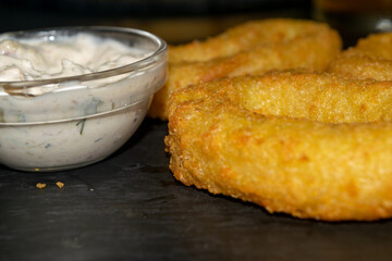 Onion rings and a glass saucepan with sauce. Close up.
