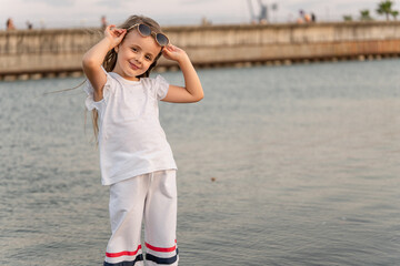 Portrait of a stylish little European girl in a white suit posing on the beach. Copy space