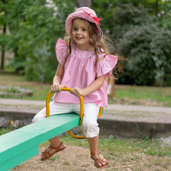 A child plays on the playground. Kid is riding on swings in the park. Charming little girl is having fun