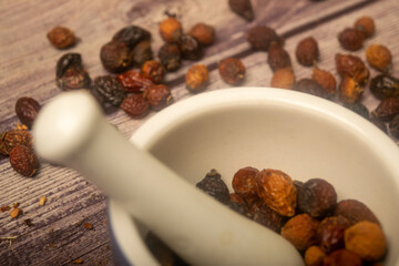 Dried rosehip fruit in a ceramic mortar and dried rosehip fruit in bulk on a wooden background. Close up.