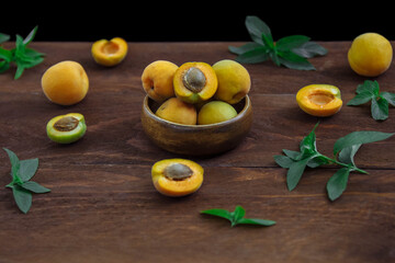 Ripe, juicy, sweet yellow apricots in a bowl whole and cut in half on a brown wooden table with...