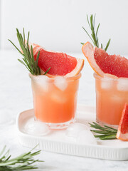 Grapefruit lemonade. Two cold wet drinking glasses with fresh grapefruit nonalcohol beverage. Ice, rosemary.