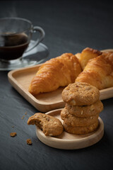 Breakfast with cookies and croissant on the wooden plate and hot coffee cup on stone table