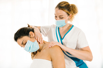 professional woman of caucasian ethnicity giving a physiotherapeutic neck massage wearing a face mask