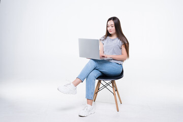 Asian businesswoman talking on the phone and looking at a laptop while sitting on a chair isolated on white background