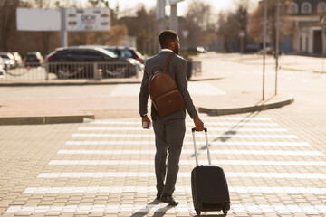 Unrecognizable Black Businessman With Suitcase Crossing Road In City, Back-View