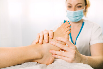 Female physiotherapy professional giving a physiotherapeutic foot massage wearing a face mask