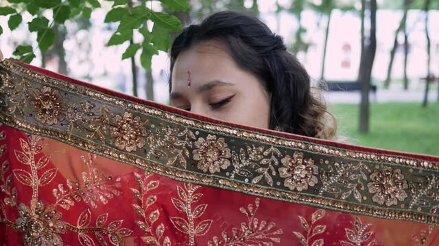 young Indian woman peeks out from behind sari and hides behind tree