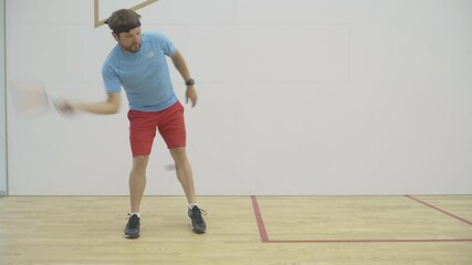 Wide shot of strong Caucasian mid-adult sportsman training in gym. Portrait of brunette bearded athletic man exercising indoors. Confident concentrated guy playing squash racket and ball sport.