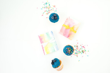 Sweet muffins, candy confetti and rainbow gift box isolated on white background. Flat lay
