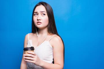 Smiling asian young woman holding takeaway coffee cup standing isolated over blue background