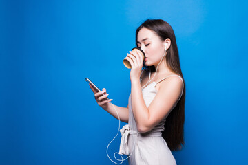 Portrait of asian young woman using mobile phone her holding coffee paper cup, looking smartphone on blue background