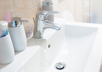 a white ceramic sink with a chromed tapa white ceramic sink with a chromed tap with soap and toothbrush containers in a bathroom. Interior of a house.