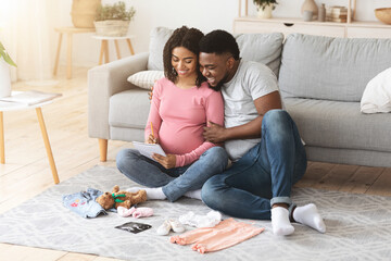 Cheerful pregnant black family preparing baby clothes and making list