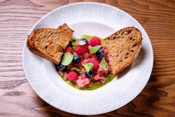 Tuna tartare with raspberries and blueberries in a white plate.